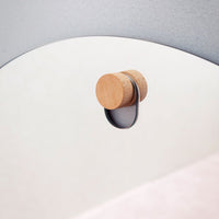 Wood and metal wall hook with a smooth gray arc and soft pink background, showcasing minimalistic design and natural tones.