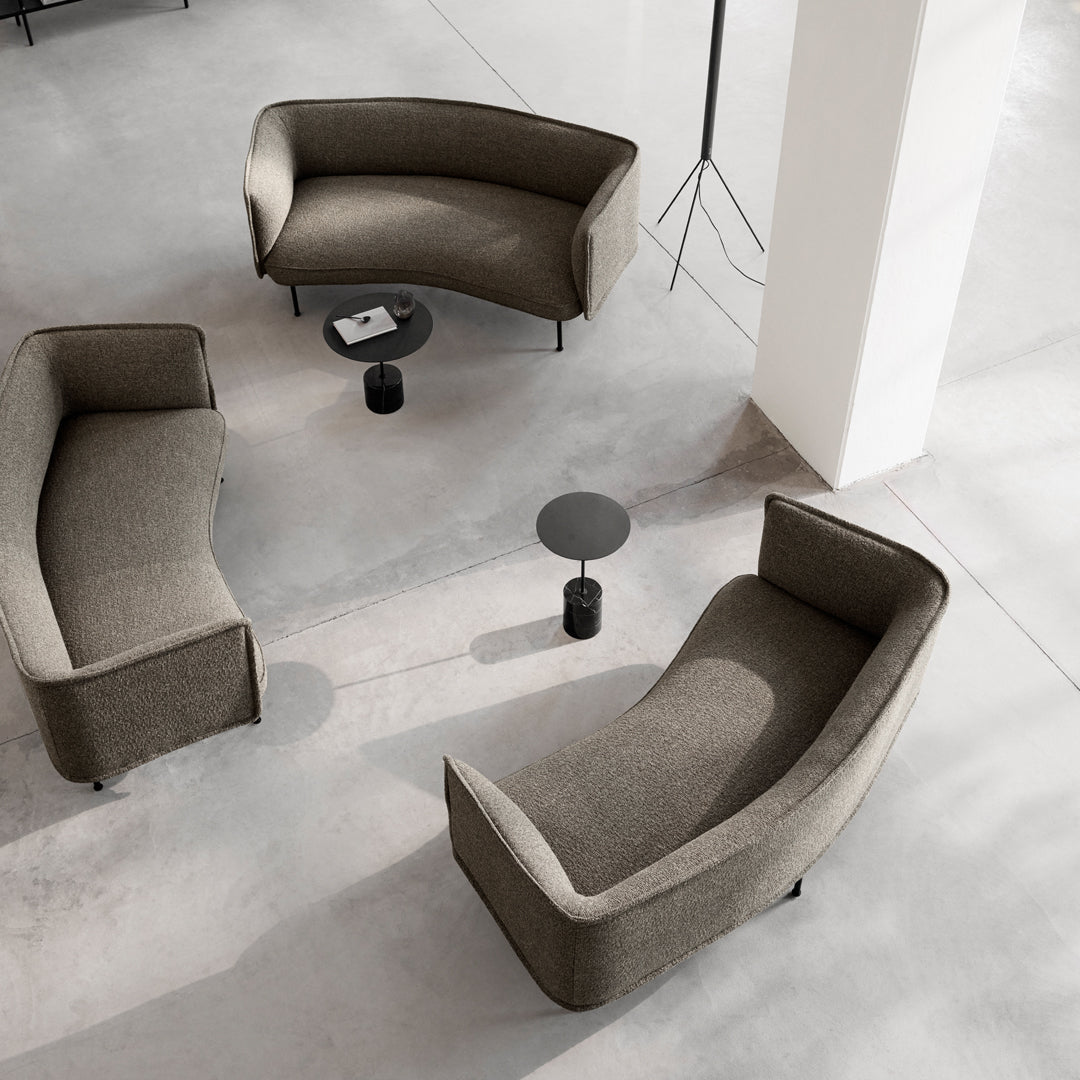 Curved modern sofas in neutral brown fabric with sleek black accents, set on a minimalist concrete floor.