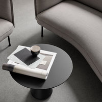 Modern black round coffee table atop a light gray floor, surrounded by muted gray upholstery and artfully arranged decor.