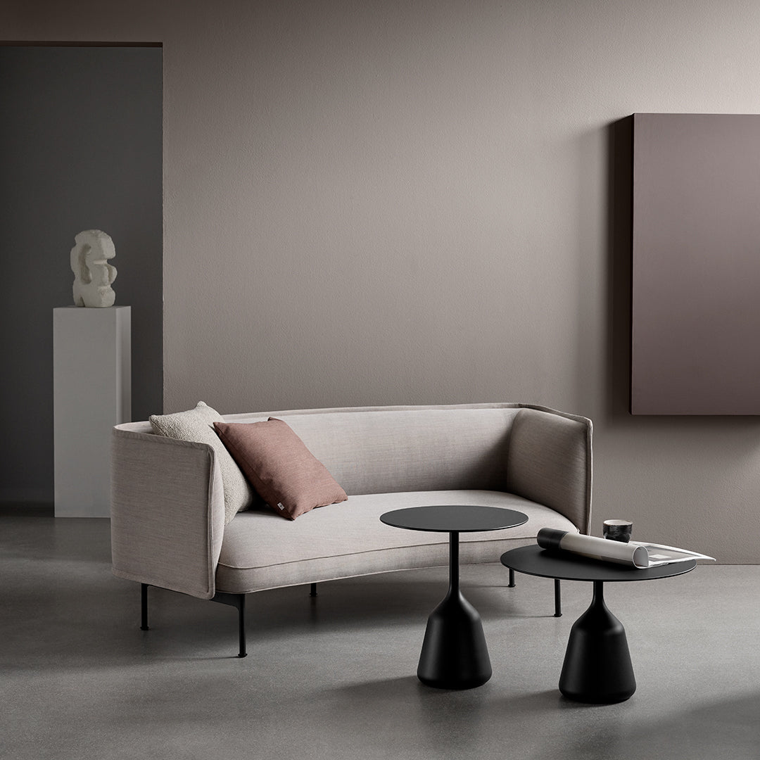 Light beige sofa with a dark cushion, paired with sleek black accent tables against a neutral backdrop.