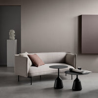 Light beige sofa with a dark cushion, paired with sleek black accent tables against a neutral backdrop.