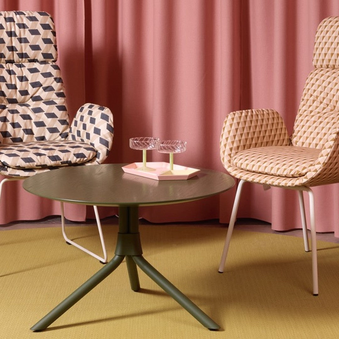 Geometric patterned chairs in shades of beige and navy, pink curtains, and a green round table on a yellow floor.