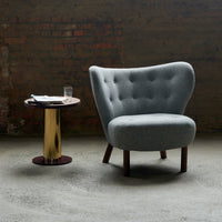 Gray tufted armchair with rounded design, paired with a sleek gold-accented side table, creating a modern aesthetic.
