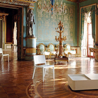 Modern white chair against an opulent turquoise wall with intricate gold patterns in a lavish interior setting.