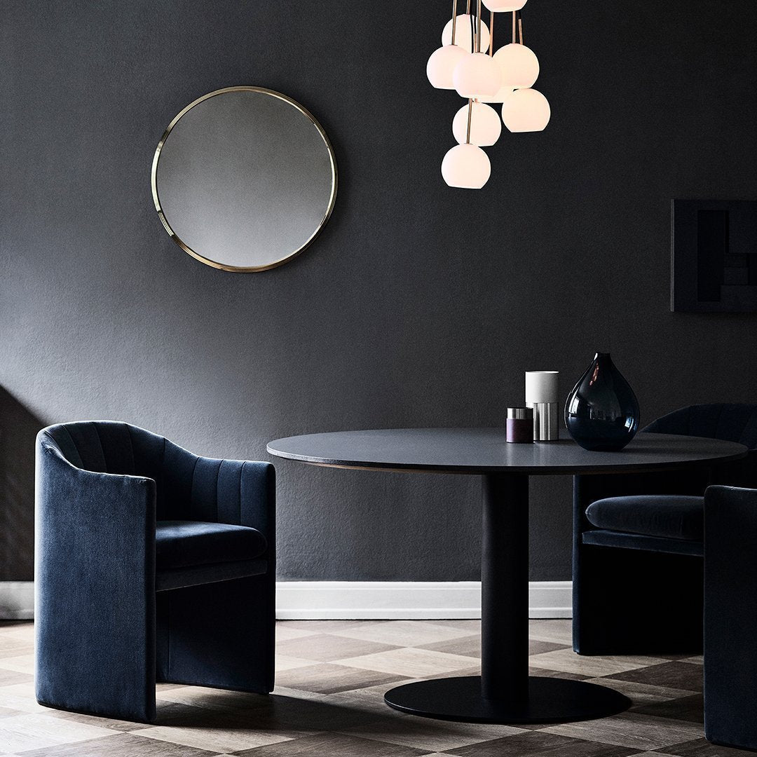 Elegant dark blue armchairs and a round black table against a sophisticated dark gray wall, featuring soft white pendant lights.