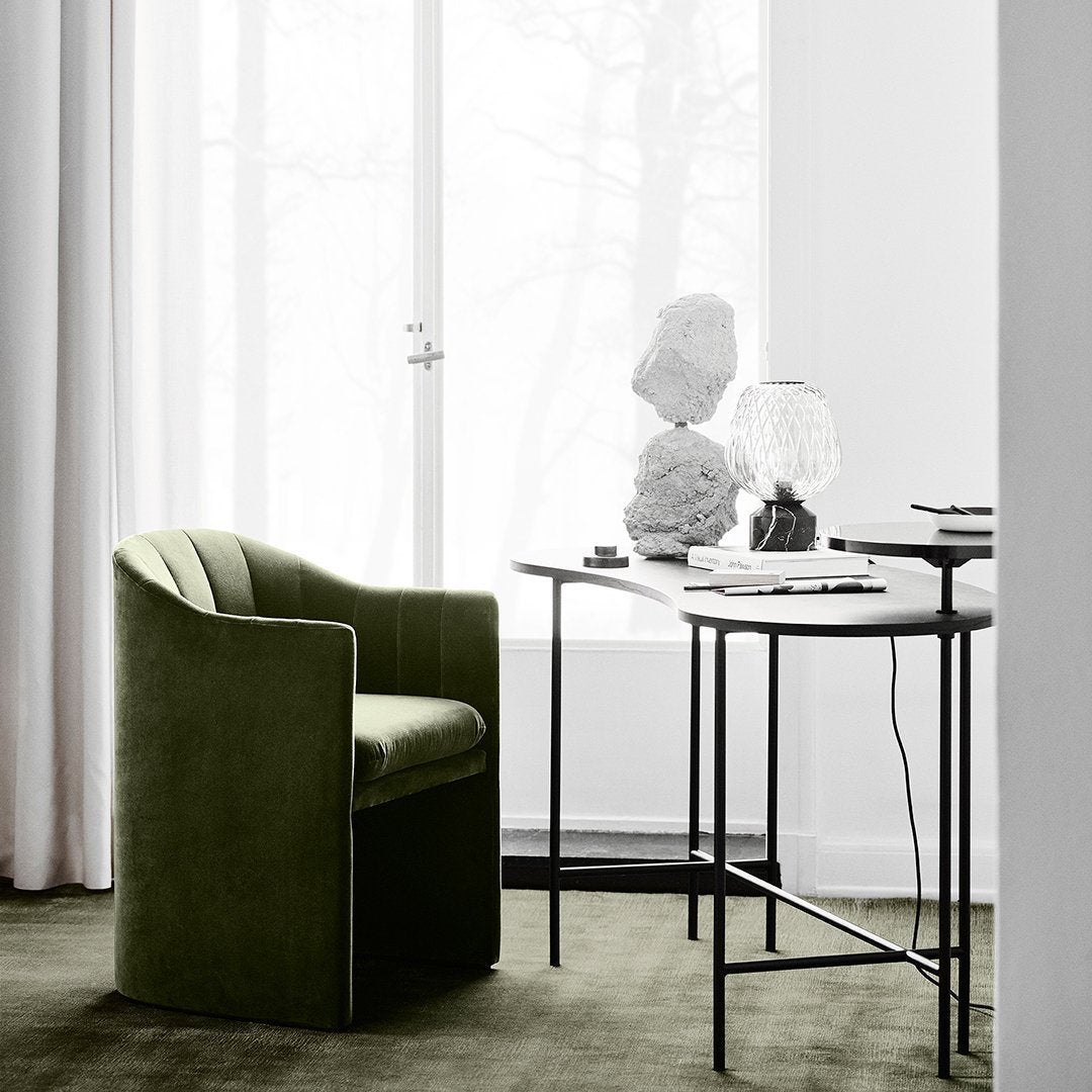 Elegant green velvet chair next to a sleek black and white table, set against a soft gray backdrop.