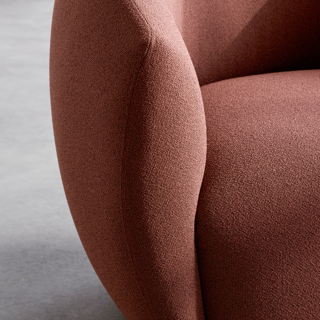 Curved rust-colored armchair with a textured, soft fabric surface, minimalistic pattern against a gray background.