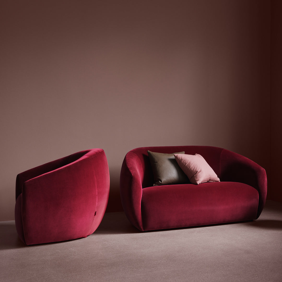 Velvet burgundy sofa and chair set with soft pink and dark green accent pillows against a muted brown backdrop.