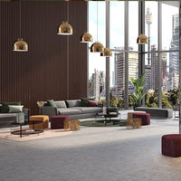 Modern living room with gray sofas, gold accents, purple and beige stools, and large windows showcasing a city view.