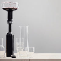 Black wine decanter with clear glassware on a light wood surface and soft grey background. Elegant and modern design.