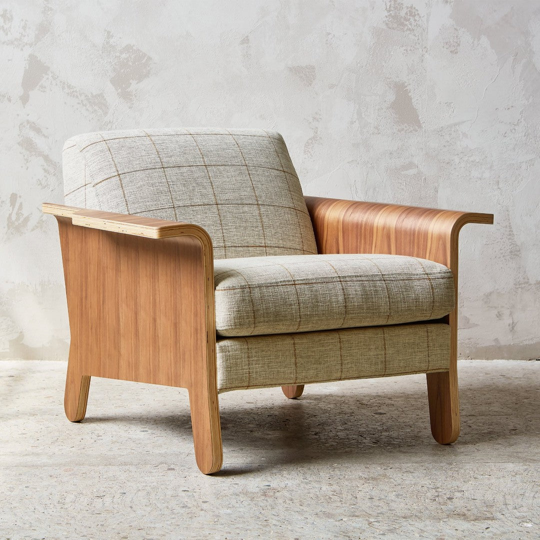 Beige plaid patterned chair with light wood arms, set against a textured neutral wall.