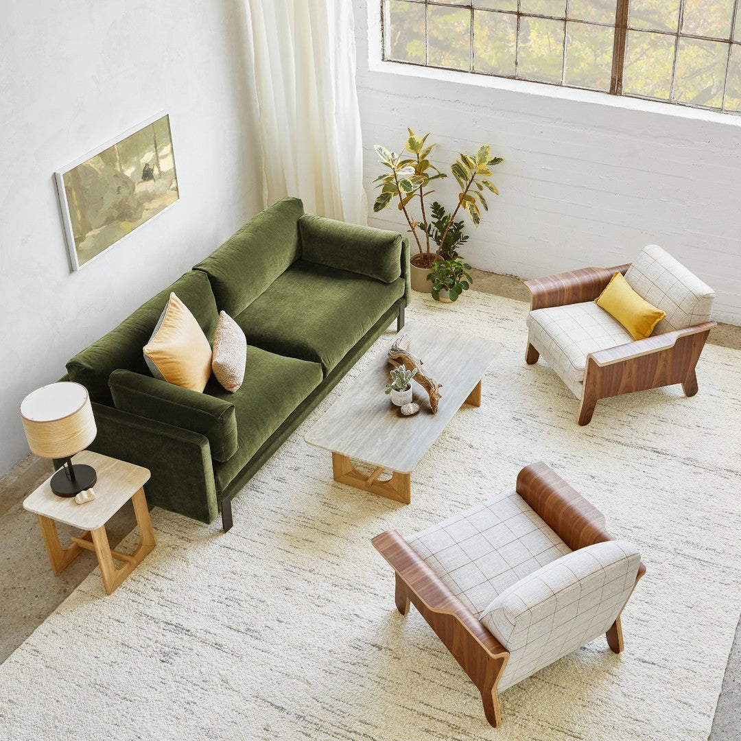 Green velvet sofa with beige and yellow pillows; light wood and checkered patterns on chairs and table.