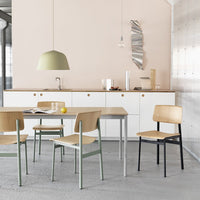 Modern dining room featuring light wood chairs with green and black accents, a soft green pendant light, and pale pink walls.