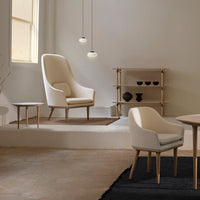 Cream and beige armchairs with light wood accents, paired with a natural wood table on a black rug in a minimalist setting.
