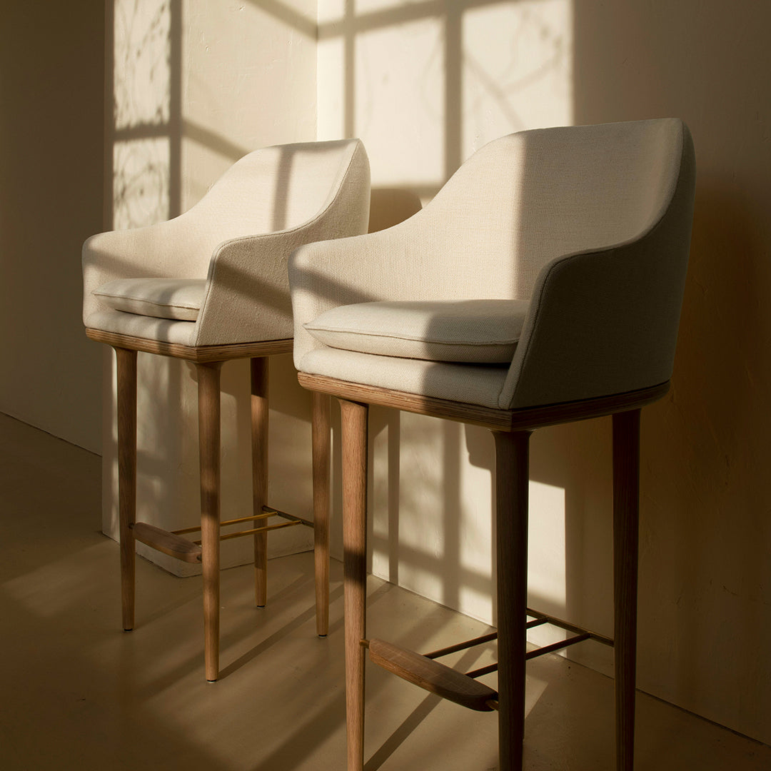 "Two cream-colored barstools with a smooth texture and wooden legs, casting soft shadows."