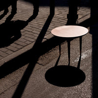 Minimalist round table in soft pink shade casting a distinct shadow on a textured pavement.