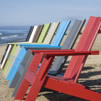 Colorful array of adirondack chairs in red, blue, green, gray, and beige, lined on a beach against a blue sky.