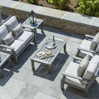 Gray outdoor furniture set with striped cushions, paired with a slatted coffee table on a stone patio.