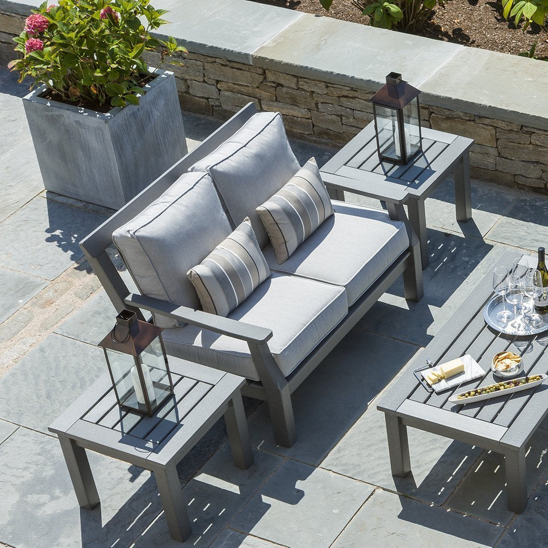 Light gray cushioned sofa with striped pillows and matching gray side tables, set against a natural stone patio.