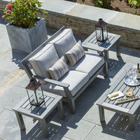 Light gray cushioned sofa with striped pillows and matching gray side tables, set against a natural stone patio.