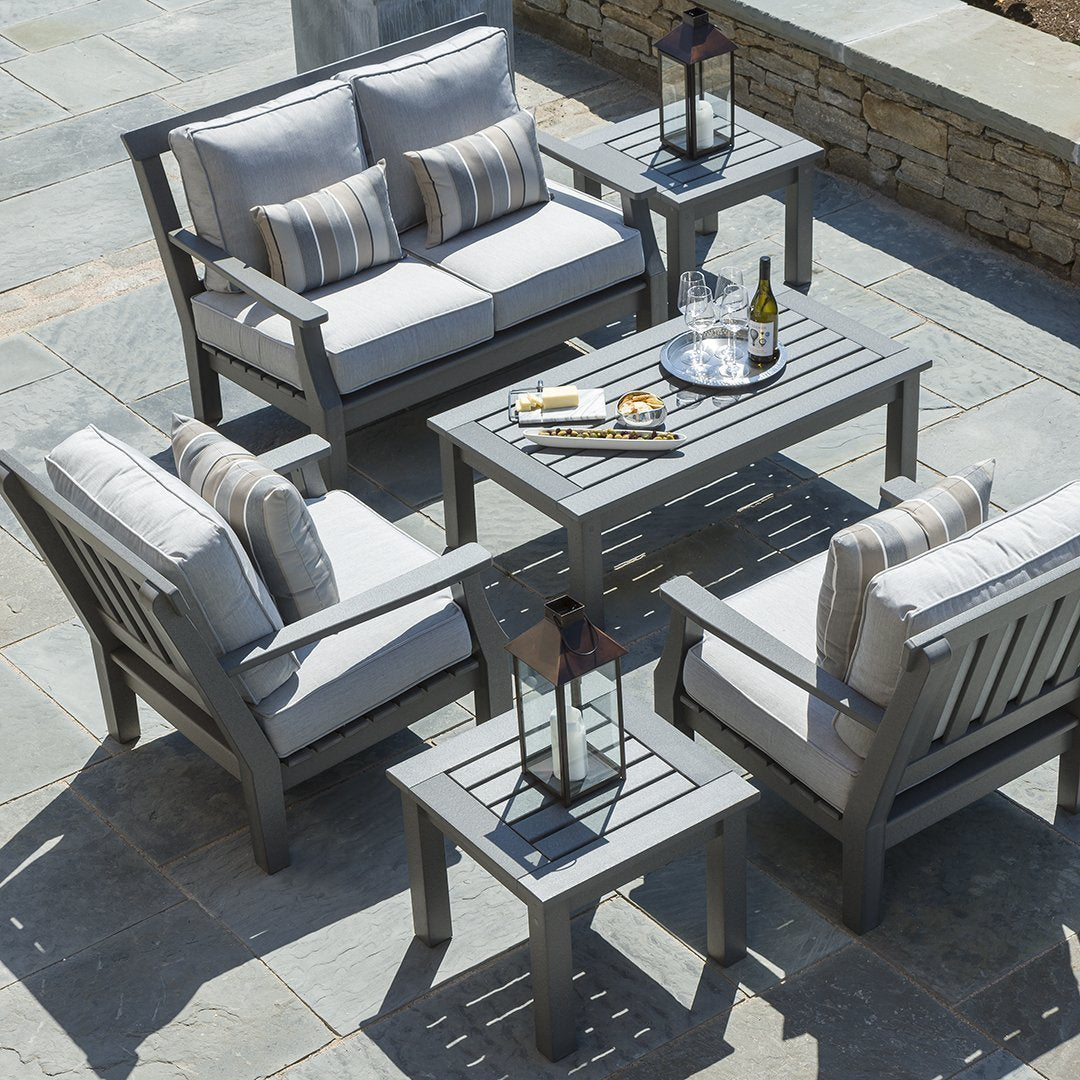 Gray outdoor furniture set with striped cushions and lanterns, featuring a sleek slatted design on a stone patio.