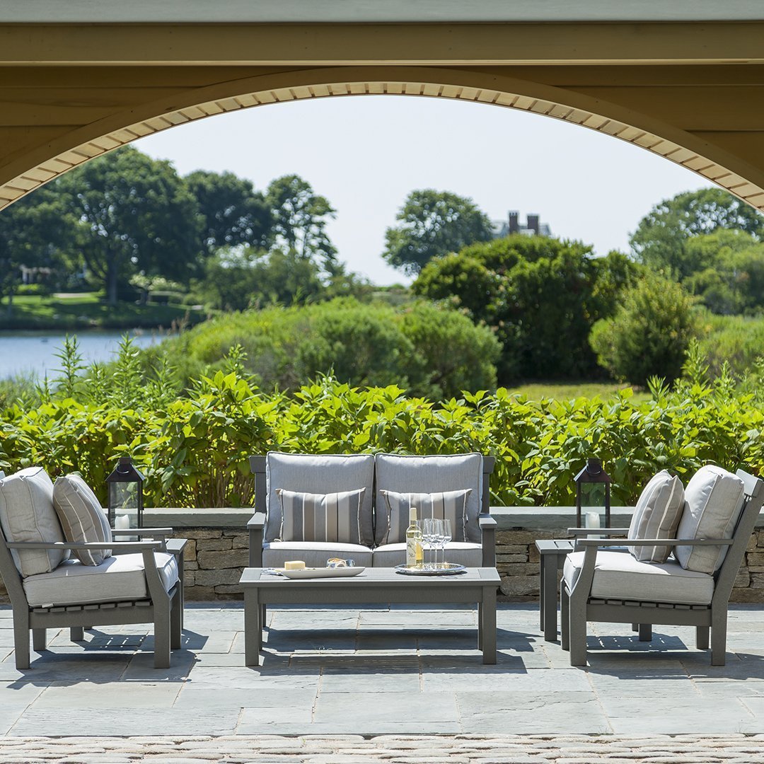 "Light gray outdoor furniture set with subtle striped cushions against a lush green landscape."
