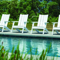 Four white Adirondack chairs lined up by a clear blue pool surrounded by lush green foliage.