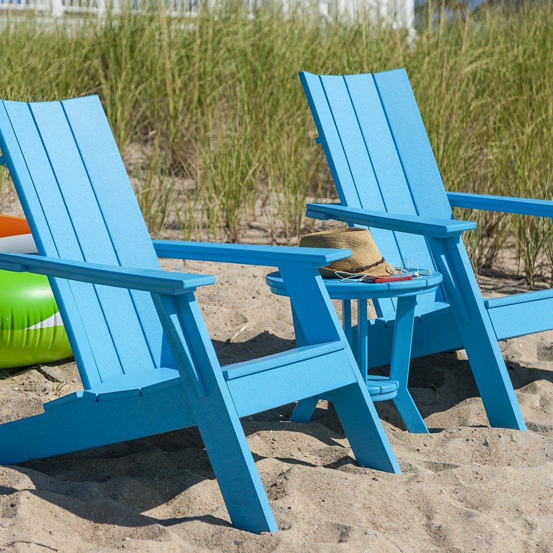 "Blue adirondack chairs on sandy beach, featuring a clean, modern design with slatted backs and matching table."