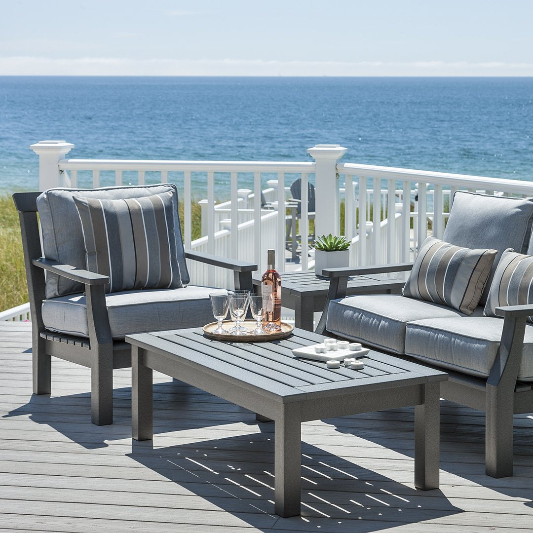 Gray outdoor furniture with blue and gray striped cushions, set against a serene seaside backdrop.