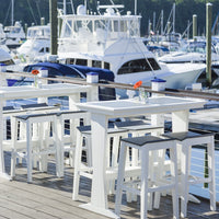 "White outdoor bar table and stools with black seats, set against a marina backdrop."