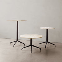Three modern tables featuring beige marble tops and sleek black metal bases, set against a minimalist backdrop.