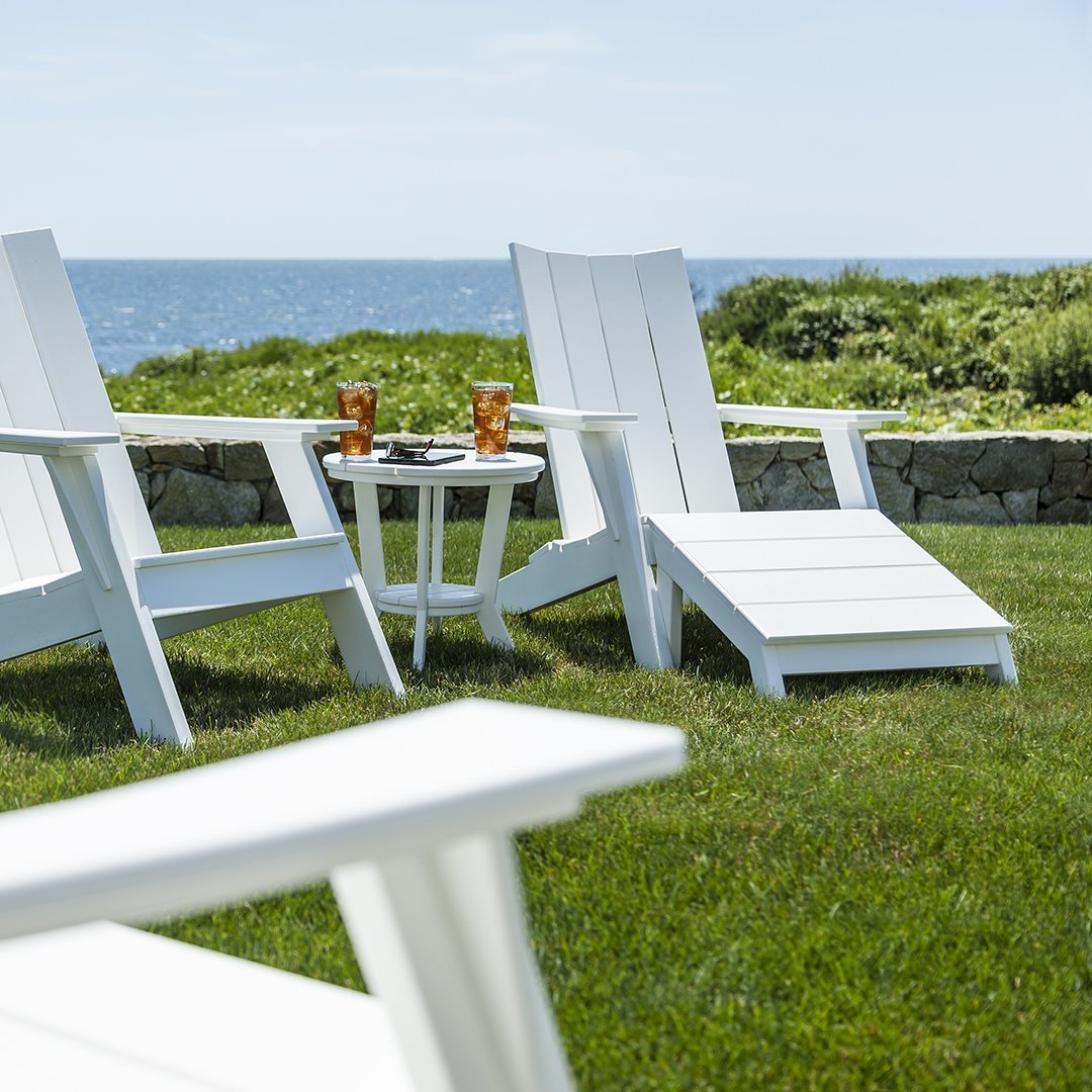 White outdoor Adirondack chairs on green grass with a scenic ocean view. Perfect for relaxation and style.