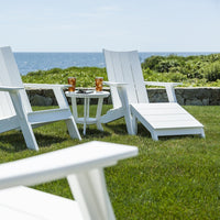 White outdoor Adirondack chairs on green grass with a scenic ocean view. Perfect for relaxation and style.
