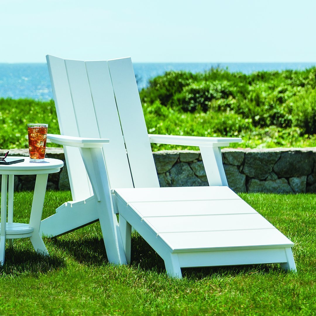 White Adirondack chair on green grass, featuring a sleek, minimalist design against a serene coastal backdrop.
