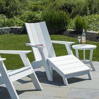 White Adirondack chairs with clean lines, paired with a round white side table on a green lawn and stone patio.