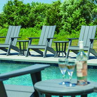 Gray outdoor adirondack chairs by a pool, set against lush greenery and a clear blue sky, featuring a simple, modern design.