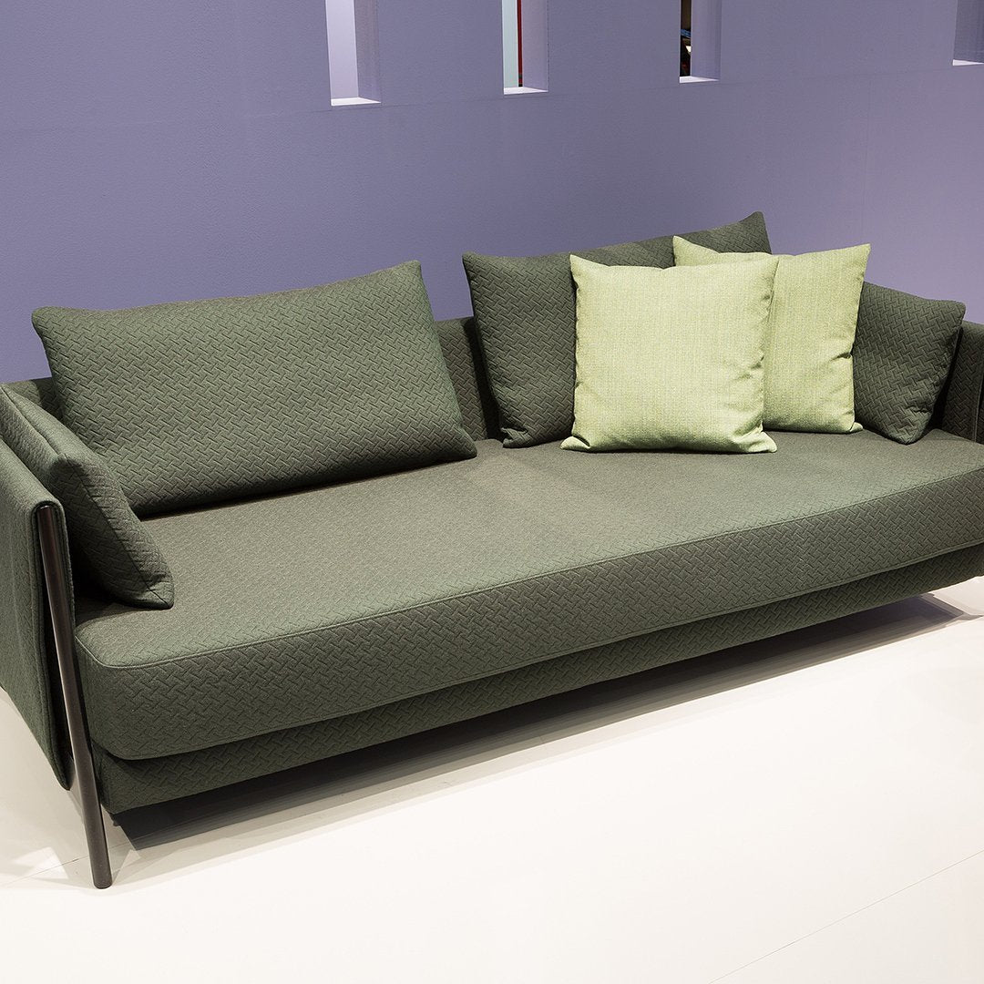 Green textured sofa with matching light green pillows, set against a soft purple background. Modern and stylish decor.
