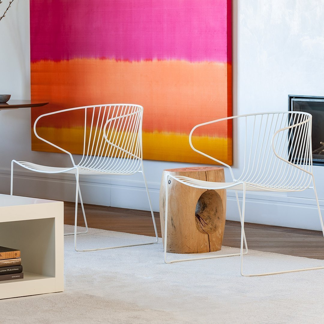 "White wire chairs against a vibrant pink and orange gradient wall, showcasing modern design and bold color contrasts."