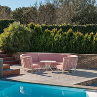 Stylish pink outdoor sofa set with minimalist white metal frame, surrounded by lush greenery and a serene blue pool.
