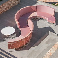 Curved pink sectional sofa with a geometric pattern and a round white table, set against a modern outdoor patio.