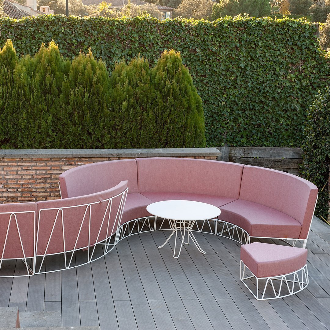 Pink curved outdoor sofa with white metal accents, complemented by a round white table and matching ottoman.