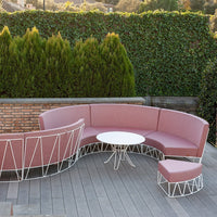 Pink curved outdoor sofa with white metal accents, complemented by a round white table and matching ottoman.