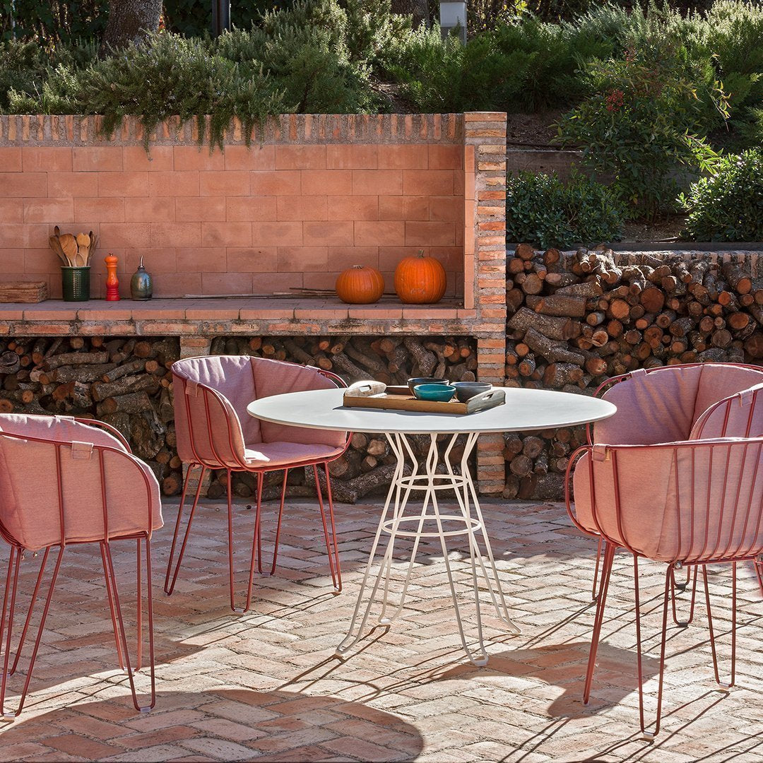 "Soft pink chairs with sleek white table against a textured brick wall and natural wood accents in a warm outdoor setting."