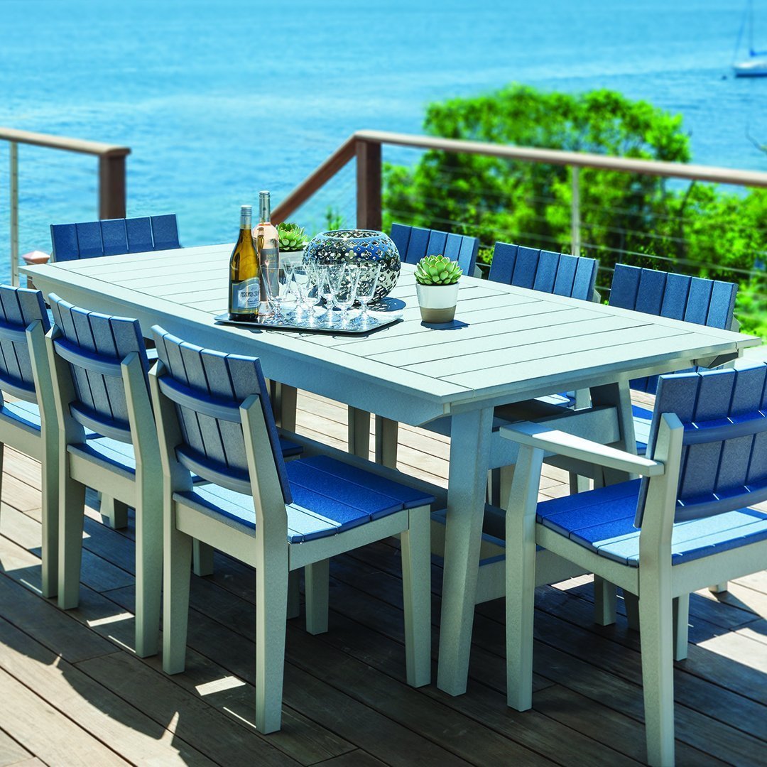 Outdoor dining set featuring a light gray table and blue slatted chairs on a wooden deck by the water.