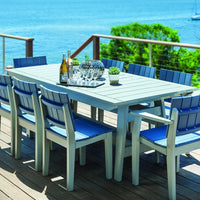 Outdoor dining set featuring a light gray table and blue slatted chairs on a wooden deck by the water.