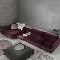 Plum velvet sectional sofa with soft gray and white accent pillows, alongside a light gray rug and black coffee table.