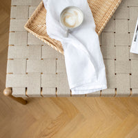 Beige woven texture on a light wooden table with a white napkin and a beige cup on a woven tray.