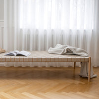 Natural wood bench with a beige woven pattern, complemented by a soft gray blanket and light curtains.