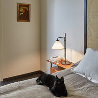 Cozy bedroom scene with neutral gray bedding, warm wooden accents, and a stylish black lamp, featuring soft textures.