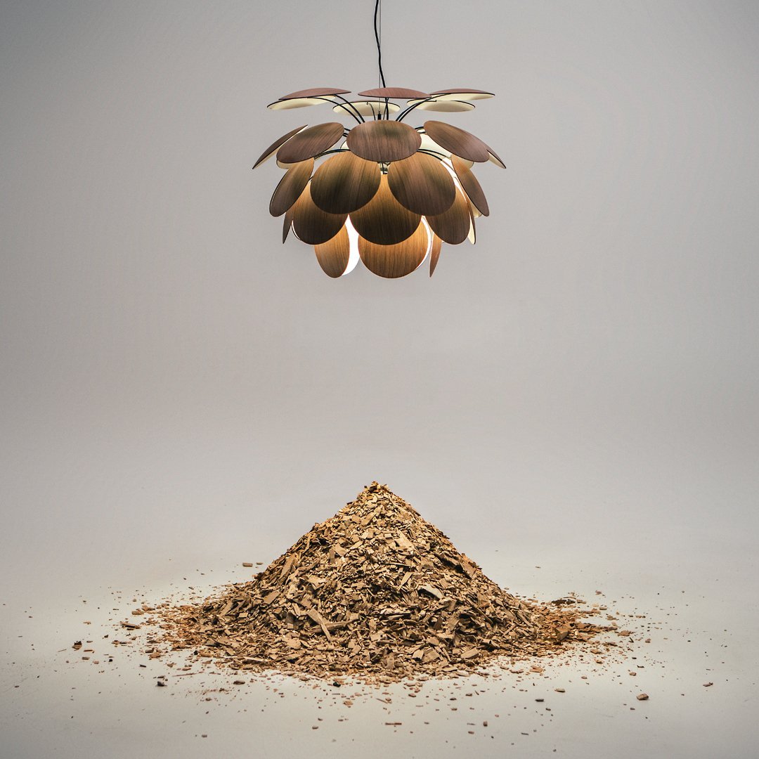 "Modern pendant light with golden scales, suspended above a textured brown mulch mound."